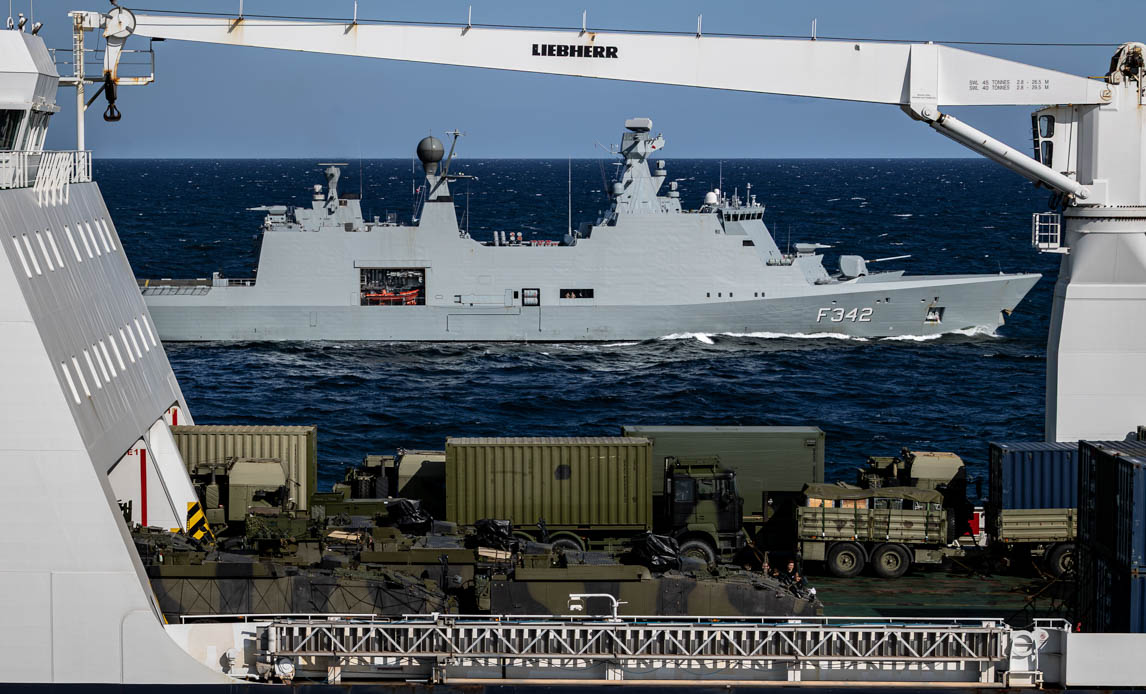 Fregat i baggrund og transportskib med materiel i forgrunden