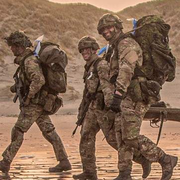 En gruppe af soldater fra Hæren marcherer på en strand, mens solen går ned.