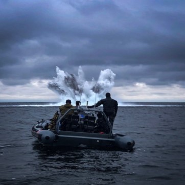 Forrest: minedykkere i gummibåd der ser på en sprængning af ammunition under vandet , som vises i baggrunden.