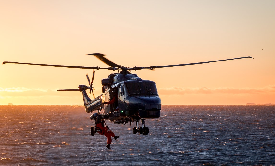 En person hænger i en slynge under en helikopter