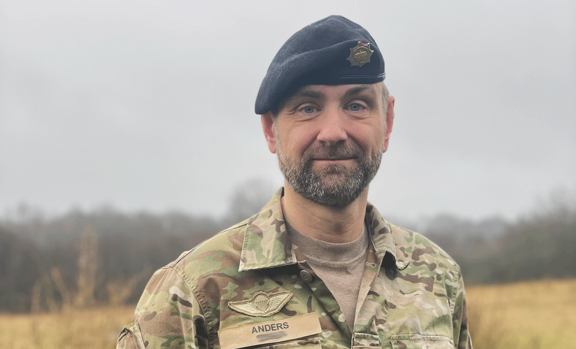 Portrætfoto af reserveofficer Anders. Han har uniform og baret på og i baggrunden er en mark.