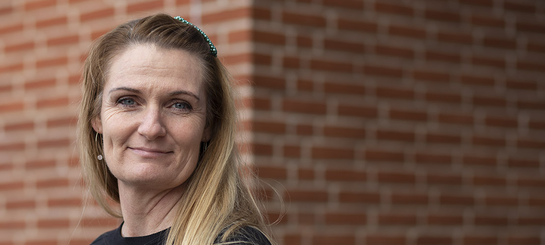 Portræt af kvindelig ansat. I baggrunden er en rød murstensbygning