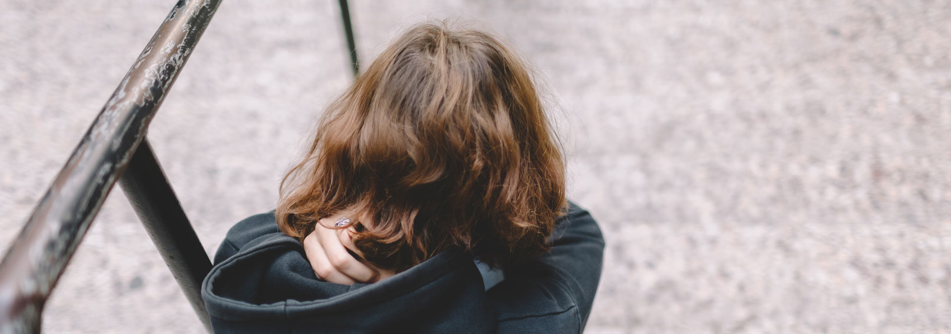 En ung kvinde sidder på en trappe med ryggen til kameraet. Hun har den ene hånd rundt om sin nakke.