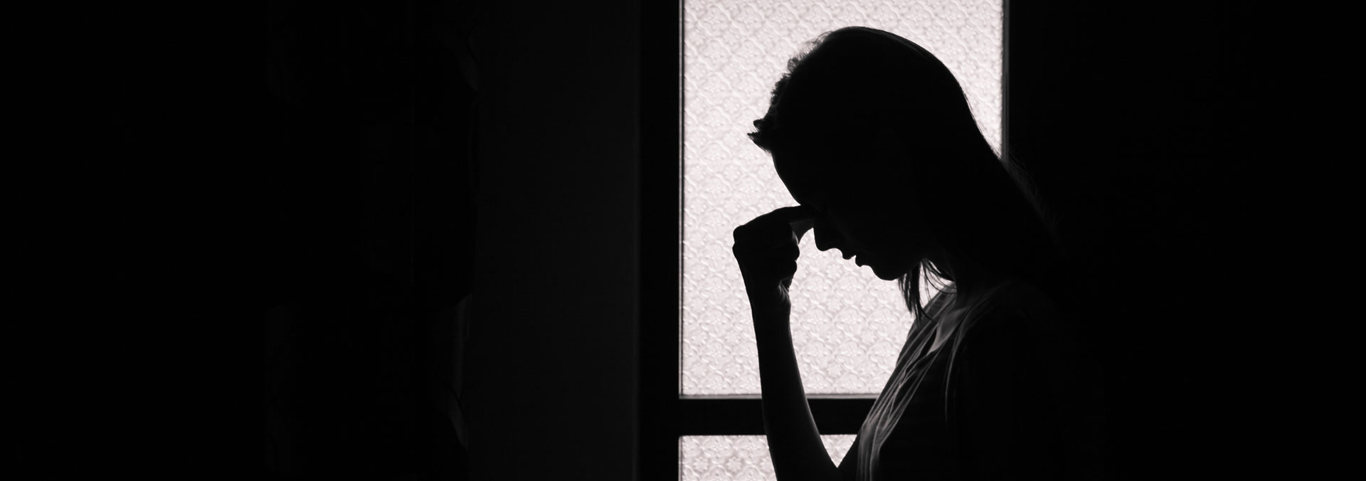 Man ser silhuetten af en kvinde, der ser deprimeret ud. Hun tager sig til hovedet